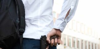 person holding a handgun behind their back near a building