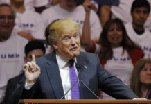 Shock Cameo Supercharges Trump Push Donald Trump speaking at a rally, gesturing with one finger raised at a podium