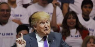 Donald Trump speaking at a rally, gesturing with one finger raised at a podium