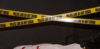 Body under white sheet with police line tape.