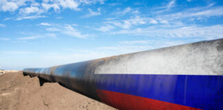 Long pipeline with Russian flag on dirt ground.