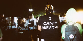 Protestor wearing I Can’t Breathe shirt facing police officers.