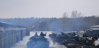 Tanks and soldiers in snowy setting near forest.
