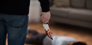 Person holding bloody knife with victim on the floor.