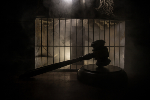 A gavel placed on a wooden surface in front of a barred cage with a smoky background