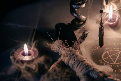A dark, mystical scene featuring candles, a voodoo doll, and occult symbols