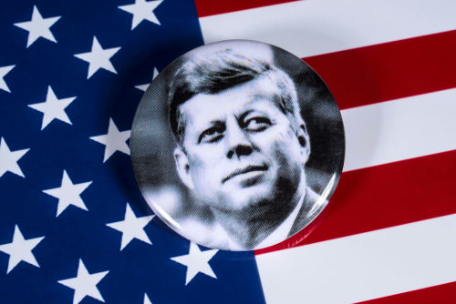 John F. Kennedy button on American flag background.