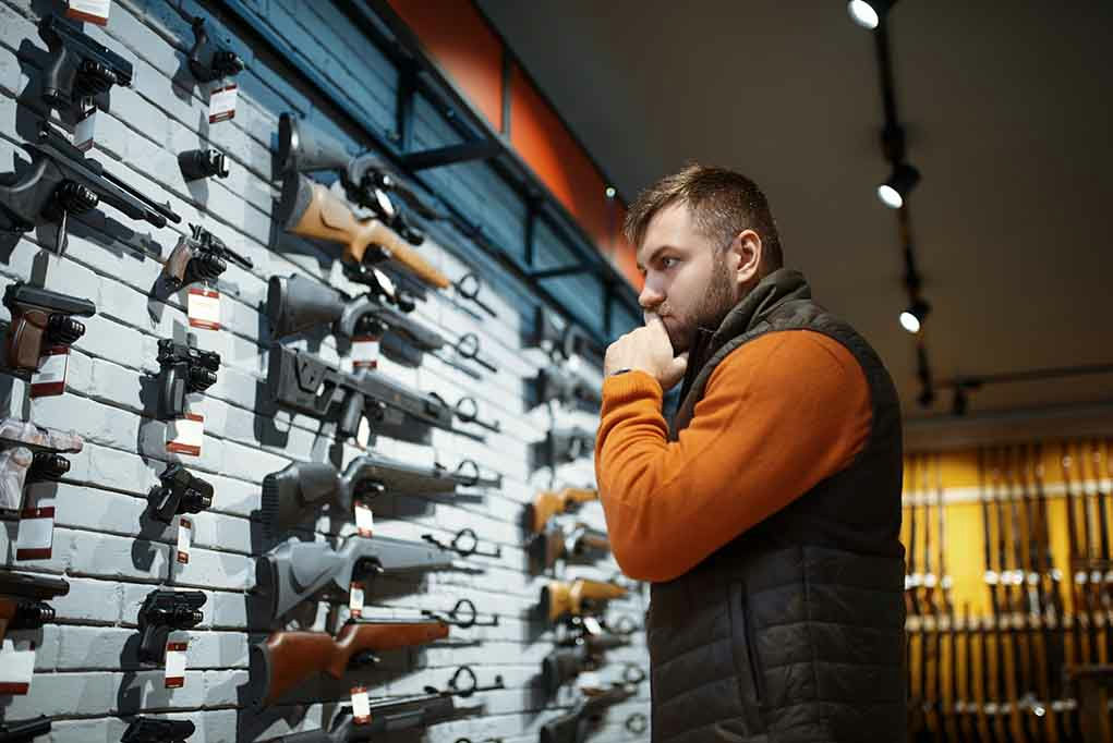 Man contemplating firearms displayed on wall.