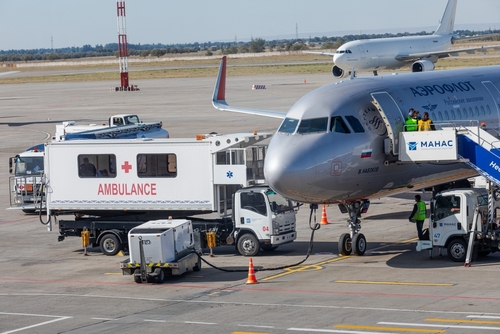 An airplane at an airport with an ambulance and ground crew nearby