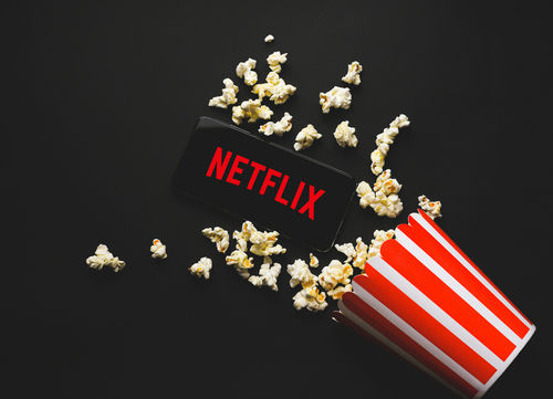 Spilled popcorn, phone displaying Netflix logo, striped popcorn container.