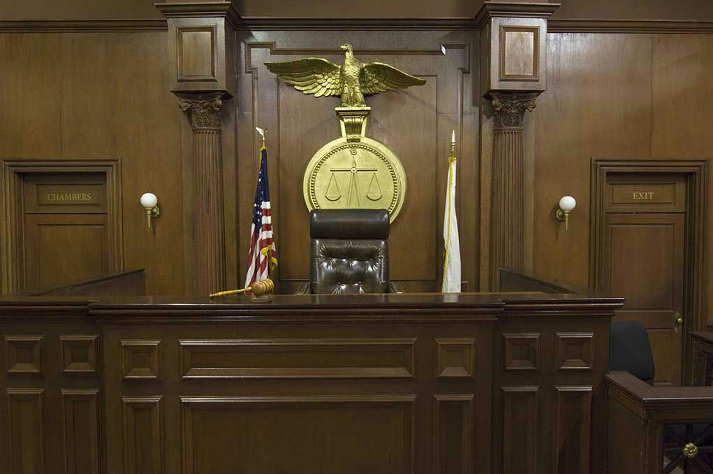 Judges bench in an empty courtroom, scales emblem above.