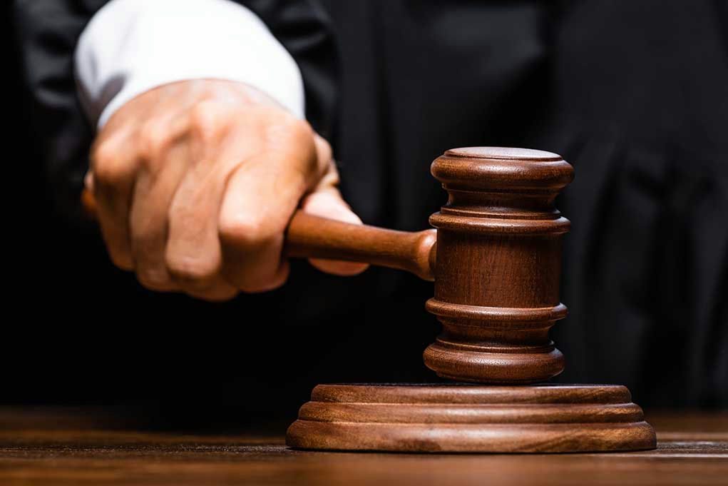 Judges hand gripping gavel on sounding block.