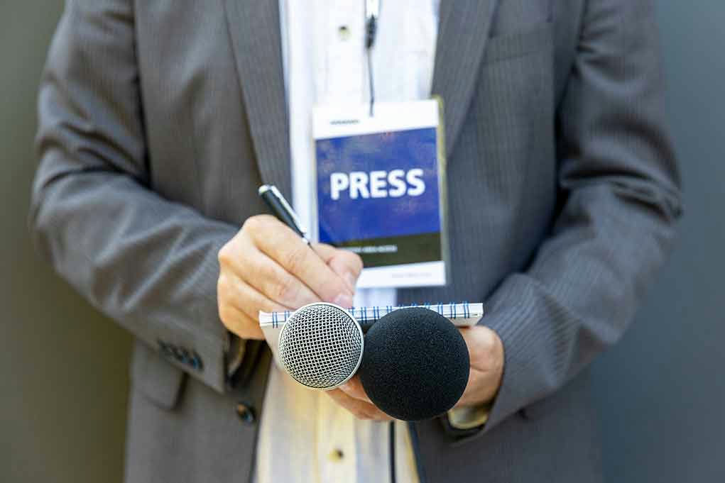 Press member holding microphones and taking notes.