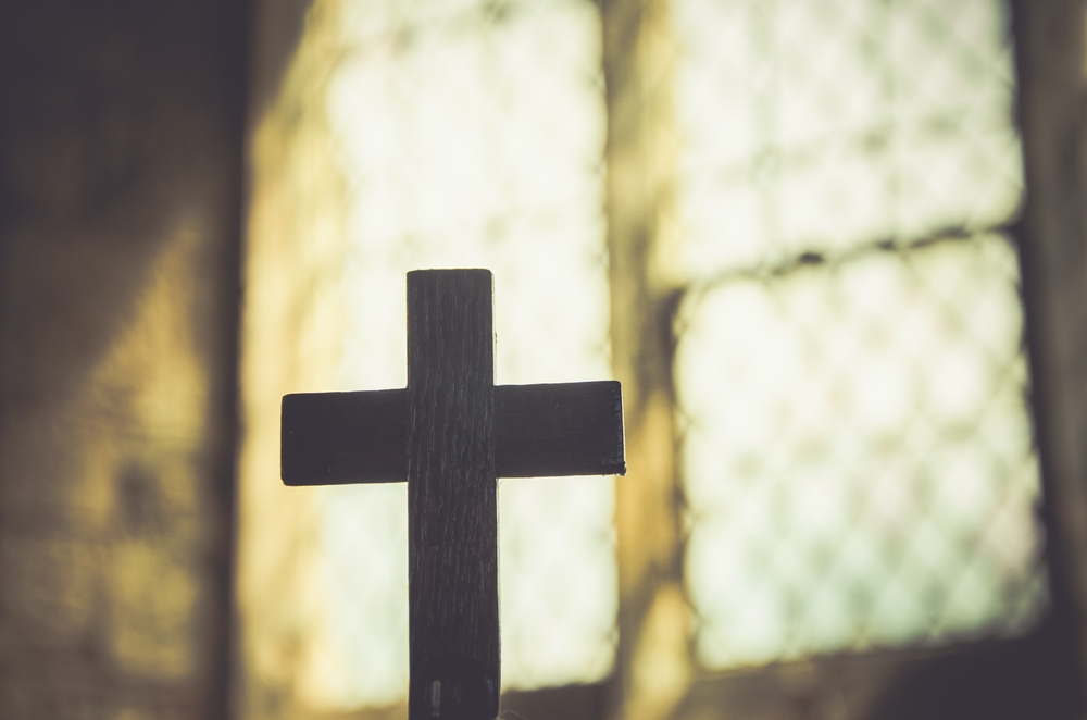 Wooden cross silhouette against a bright stained-glass window