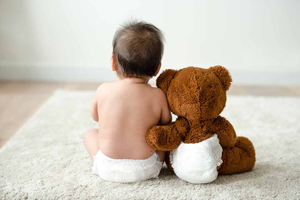 Baby in diaper sitting with teddy bear